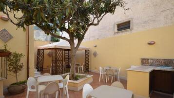 An outdoor patio with white tables and chairs, a small tree, and a tiled backsplash.
