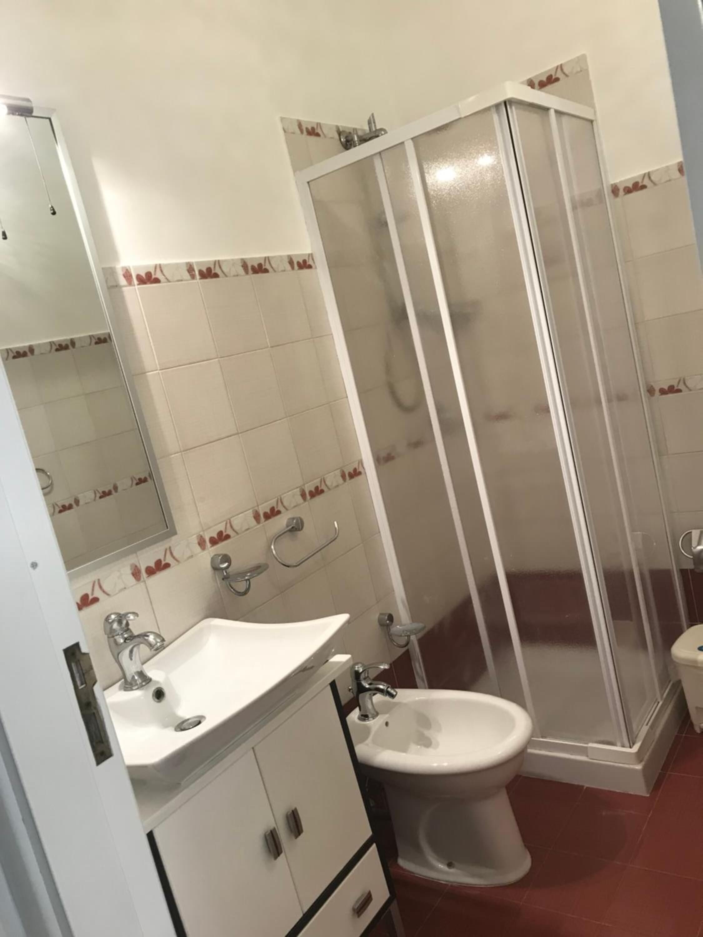 Un baño con lavamanos blanco, inodoro y cabina de ducha con mampara de vidrio.