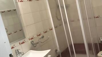 Un baño con lavamanos blanco, inodoro y cabina de ducha con mampara de vidrio.