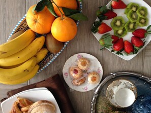 Una mesa con diversas frutas, como plátanos, naranjas, fresas y rodajas de kiwi, junto con pasteles y un plato decorativo.