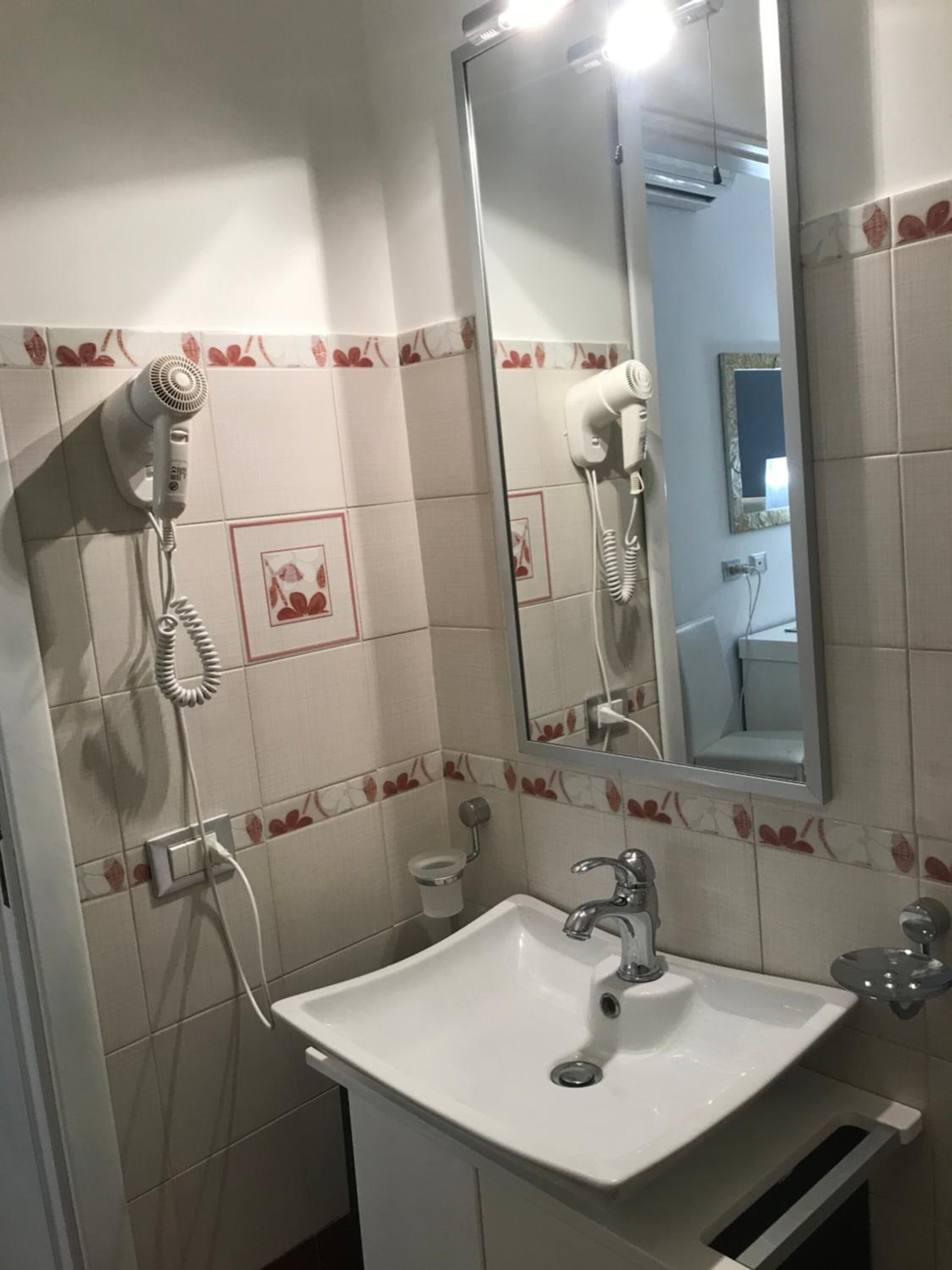 A bathroom with a white sink, a mirror, and a hairdryer mounted on the wall.