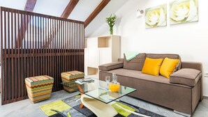 Un salon moderne avec un canapé marron, des poufs colorés, une table basse en verre et un mur décoratif orné d’œuvres d’art encadrées.