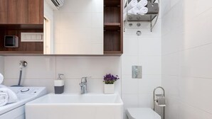 Une salle de bain moderne équipée d’un lave-linge intégré, d’une grande baignoire, de toilettes et d’un porte-serviettes.