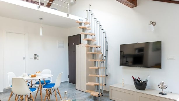 Un salon moderne doté d’un escalier en colimaçon, d’un coin repas avec une table en verre et d’un téléviseur à écran plat fixé au mur.