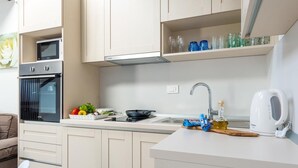 Une cuisine moderne équipée d’un four encastré, d’un évier et d’un four à micro-ondes. On y trouve des placards au-dessus du plan de travail et une étagère où sont rangés des verres.