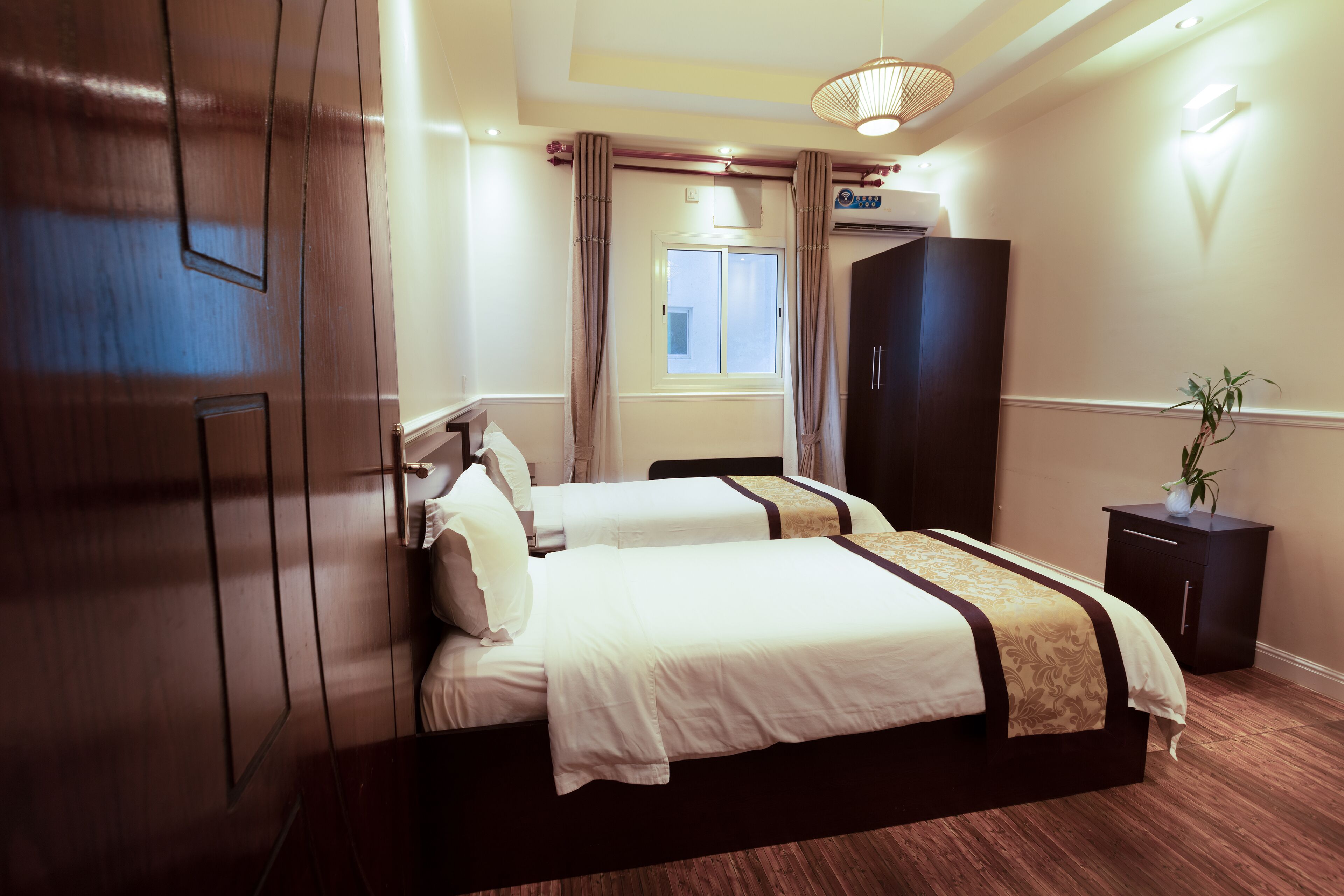 A hotel room with a large bed, a wardrobe, a bedside table, and a window with curtains.