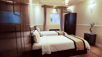A hotel room with a large bed, a wardrobe, a bedside table, and a window with curtains.