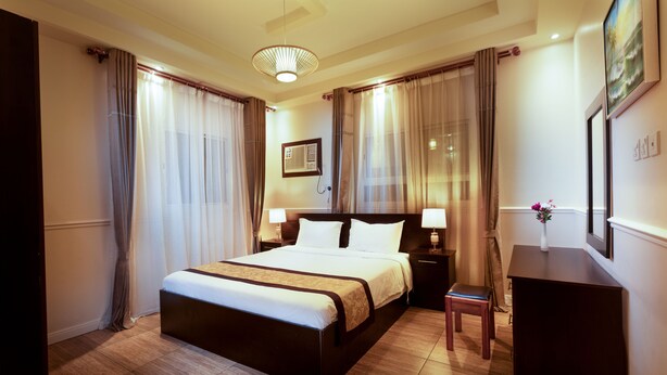 A hotel room with a large bed, bedside tables with lamps, a desk, and a chair. - Gardens View Serviced Apartment  (Taif)