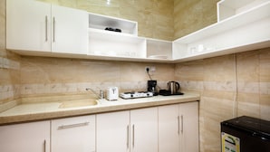 A modern kitchen with white cabinetry, a countertop with a sink, a coffee maker, and a black refrigerator. - Gardens View Serviced Apartment  (Taif)