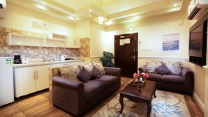 A modern living room with two sofas, a coffee table, and a kitchen area with white cabinets and a tiled backsplash. - Gardens View Serviced Apartment  (Taif)
