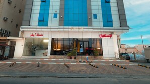 A tall hotel with a modern design, featuring a prominent blue and white facade, and a ground-level entrance with a glass facade. - Gardens View Serviced Apartment  (Taif)