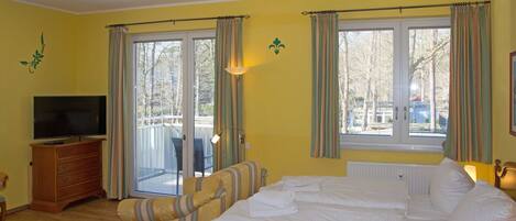 A bedroom with a bed, a television, a chair, and a window with curtains.