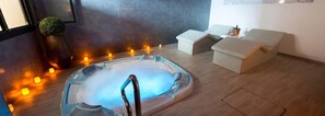 Un jacuzzi con luz azul, rodeado de velas, una planta pequeña y un banco de mimbre.