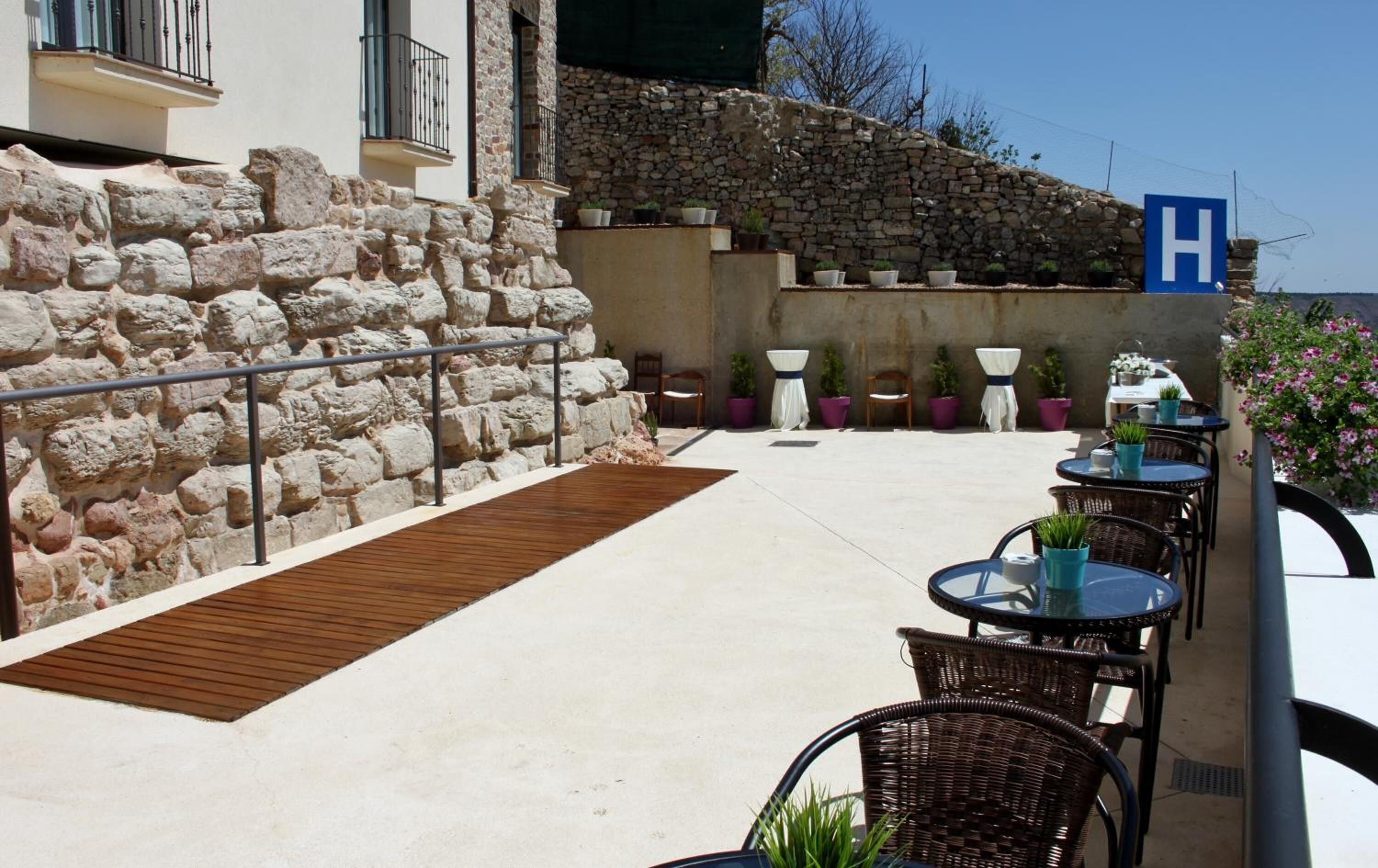 Un patio al aire libre con muros de piedra, piso de madera y mobiliario de mimbre.