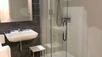 Un bany modern amb plat de dutxa de vidre, un lavabo blanc i un petit tamboret.