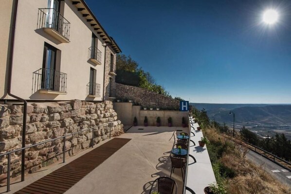 Un edificio con fachada de piedra, zona de estar al aire libre con mesas y sillas, y vistas al paisaje.