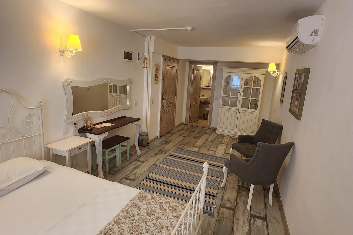 Une chambre à coucher avec un lit, un bureau, une chaise et une armoire. On peut apercevoir une salle de bain à travers une porte ouverte.