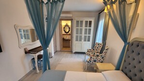 A bedroom with a large bed, a nightstand, a chair, a wardrobe, and a bathroom visible through an open door.