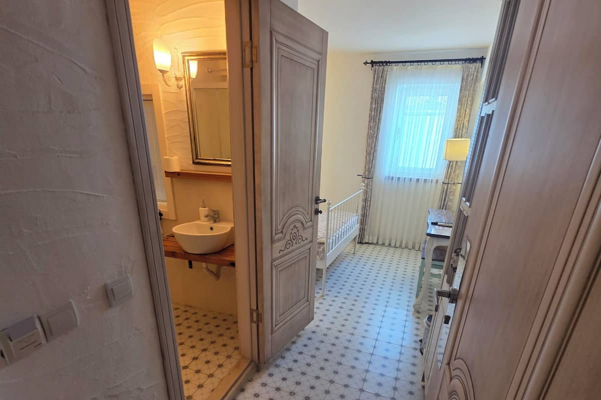 Un couloir avec des carreaux de sol à motifs, une porte en bois et une salle de bain visible à travers une porte ouverte.