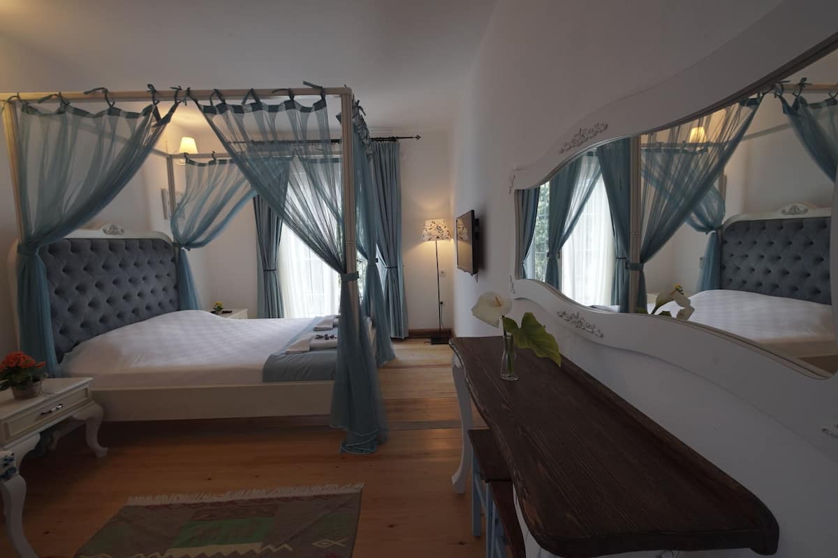 Une chambre à coucher avec un lit à baldaquin, une table de chevet, un miroir et un banc en bois.