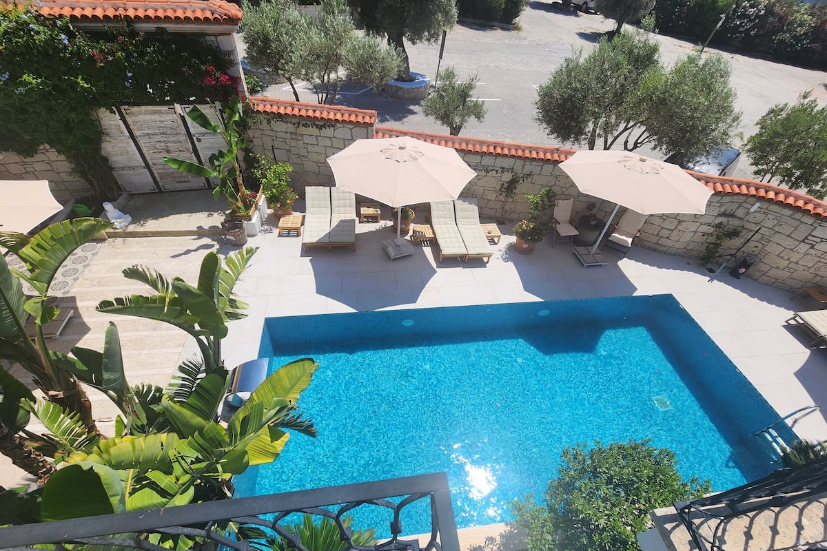 Une piscine entourée de murs de pierre et de verdure, avec des chaises longues et des parasols.