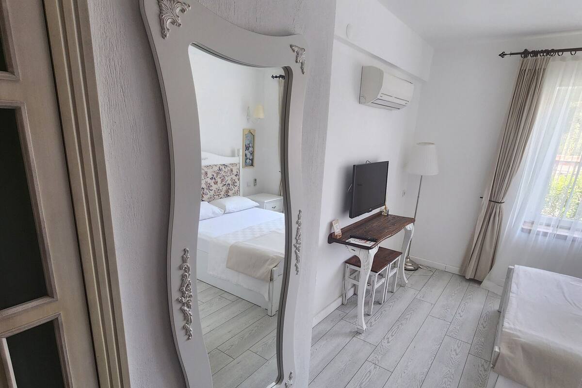Une chambre d’hôtel avec un lit, un bureau, une télévision et un grand miroir.