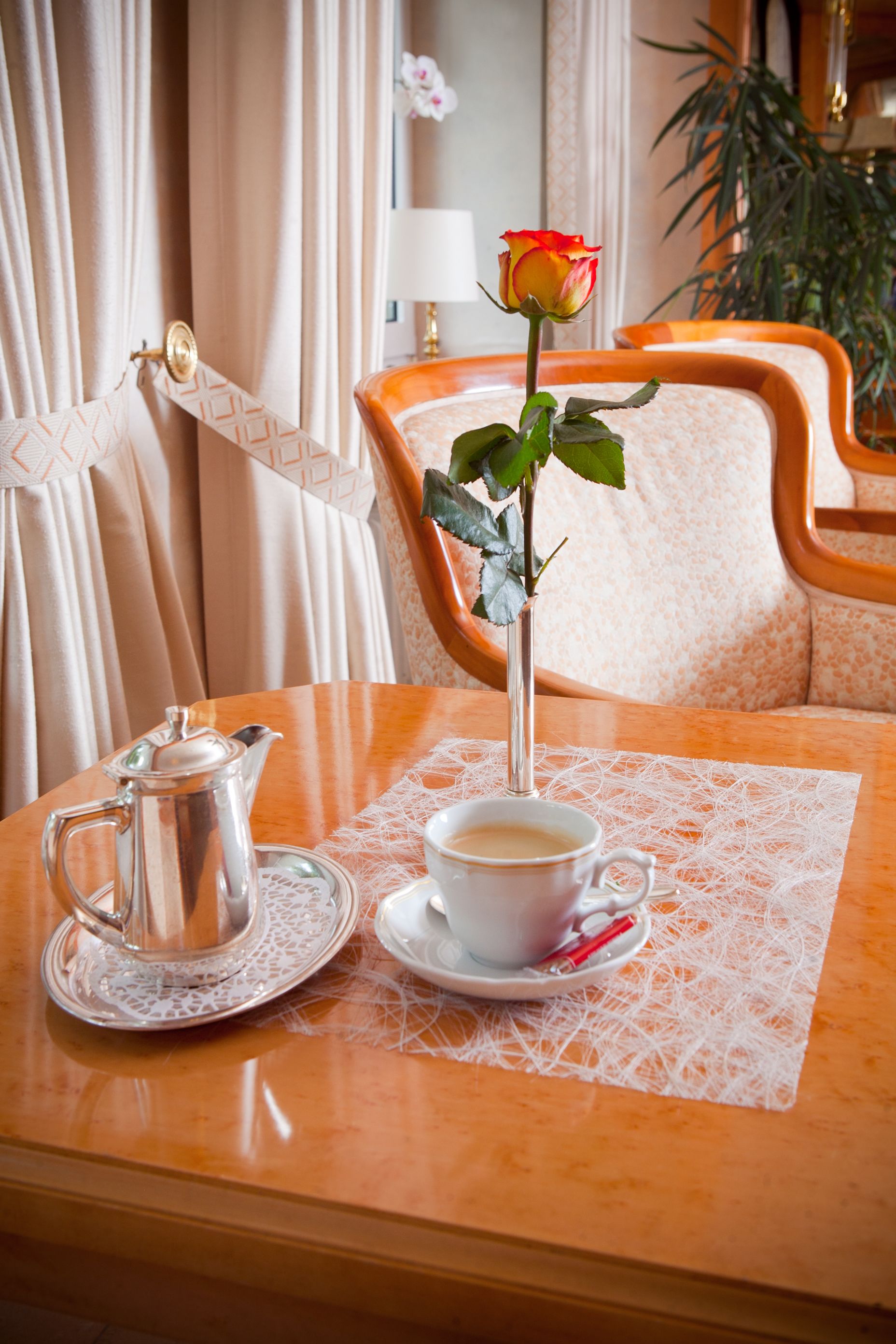 A table with a coffee cup, a teapot, and a rose in a vase.