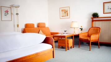 Habitación de hotel con una cama grande, dos sillones naranja, una mesita de noche con lámpara y un radiador.