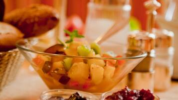 A bowl of fruit salad with a spoon, surrounded by various condiments and pastries on a table.