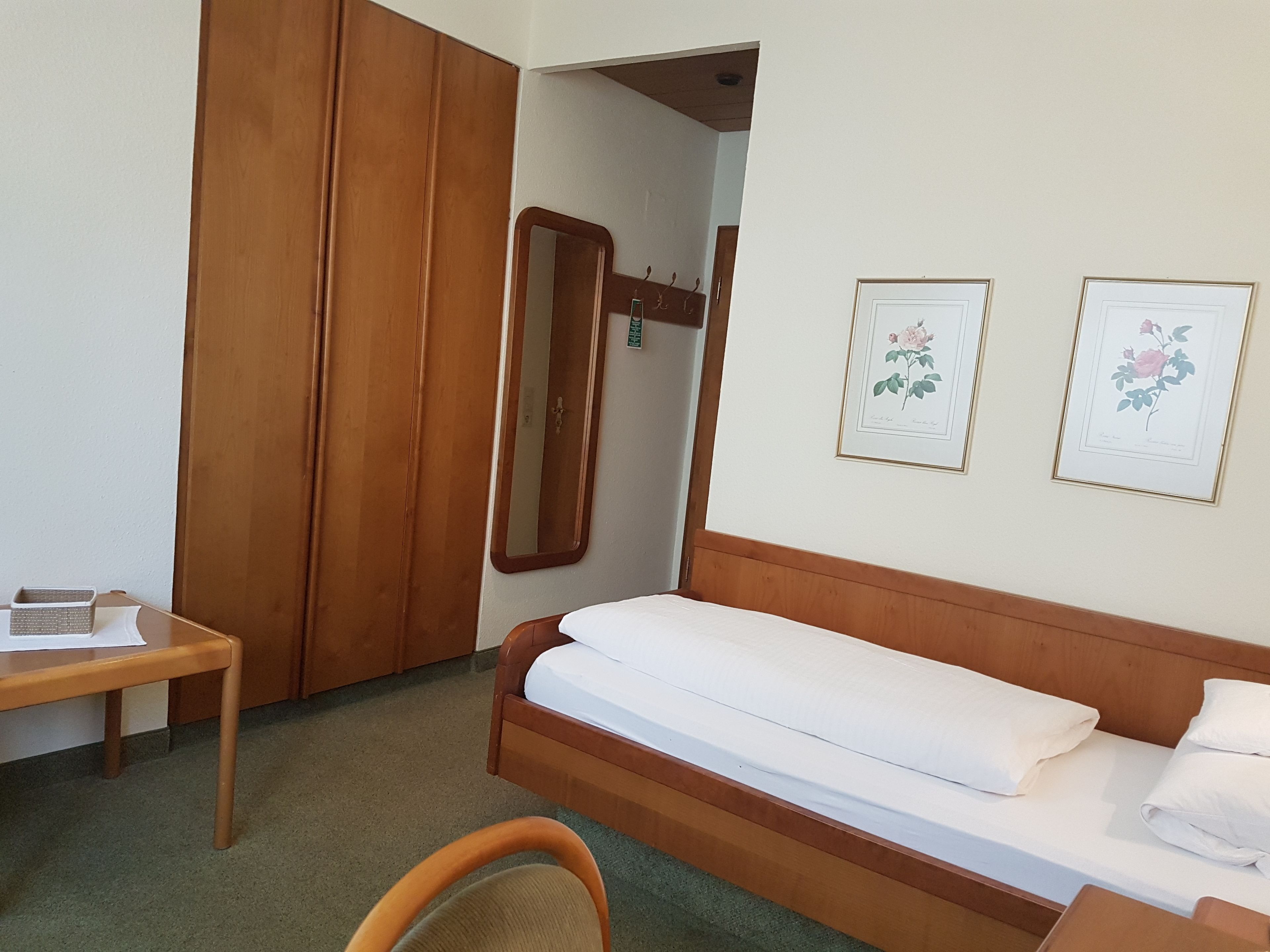 A bedroom with a wooden bed, a bedside table, a chair, a wardrobe, and two framed floral pictures on the wall.