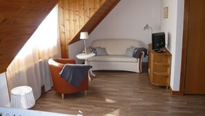 Una habitación cálida en el ático con techo de madera, un sofá, una mesita, un televisor y un armario de madera.