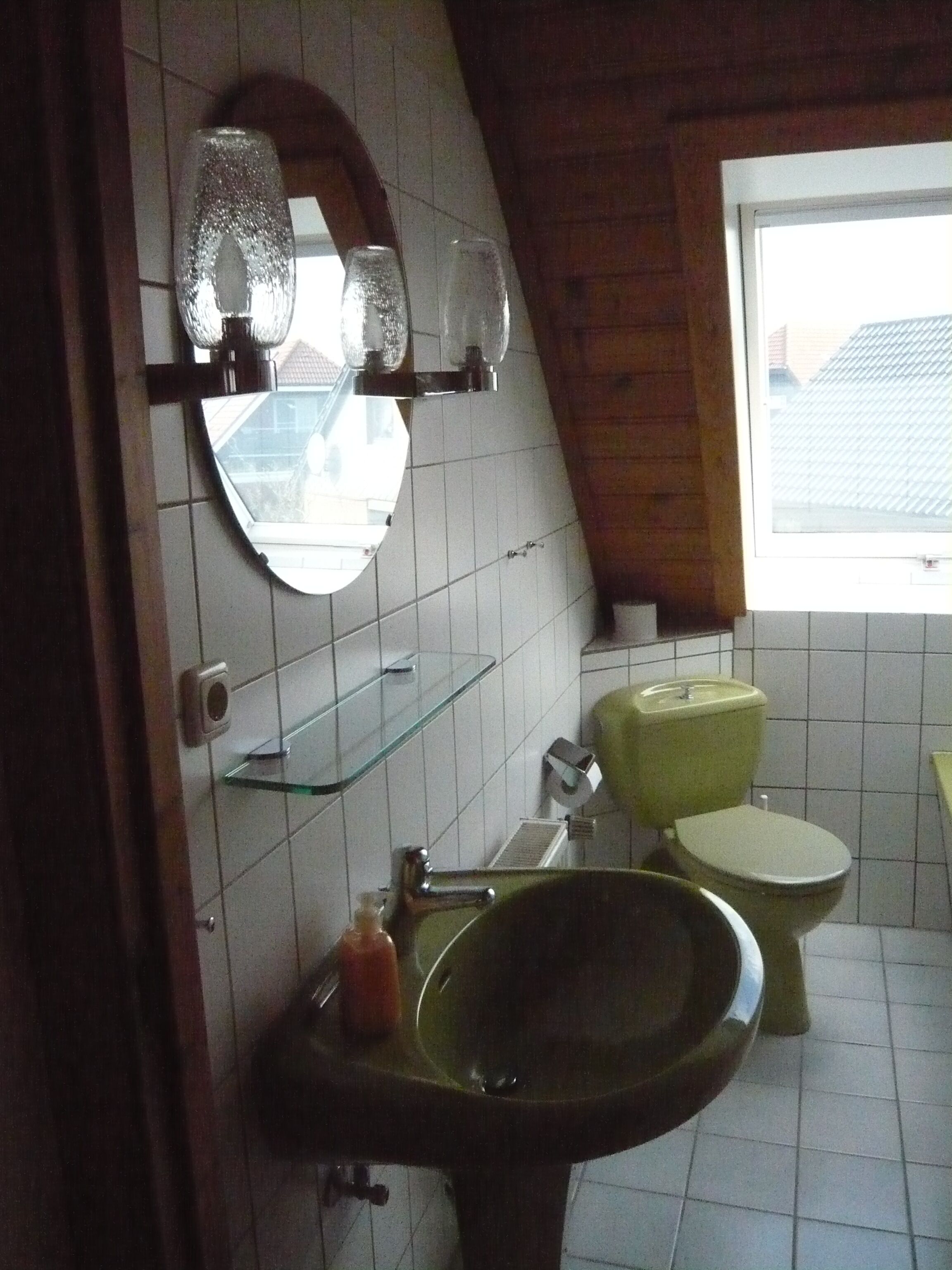 A bathroom with a green sink, a toilet, and a mirror.