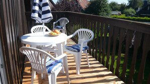 Una terraza de madera con sillas de plástico blanco y una mesa, un paraguas a rayas y un plato de fruta.