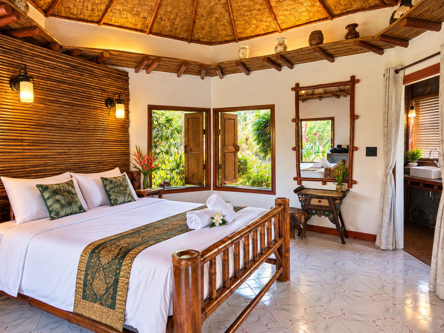 A hotel room with a bed, a wooden headboard, a mirror, a vanity, and a window with a view of greenery.