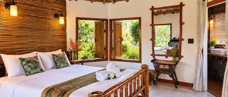Habitación de hotel con cama, cabecero de madera, espejo, tocador y ventana con vista a la vegetación.