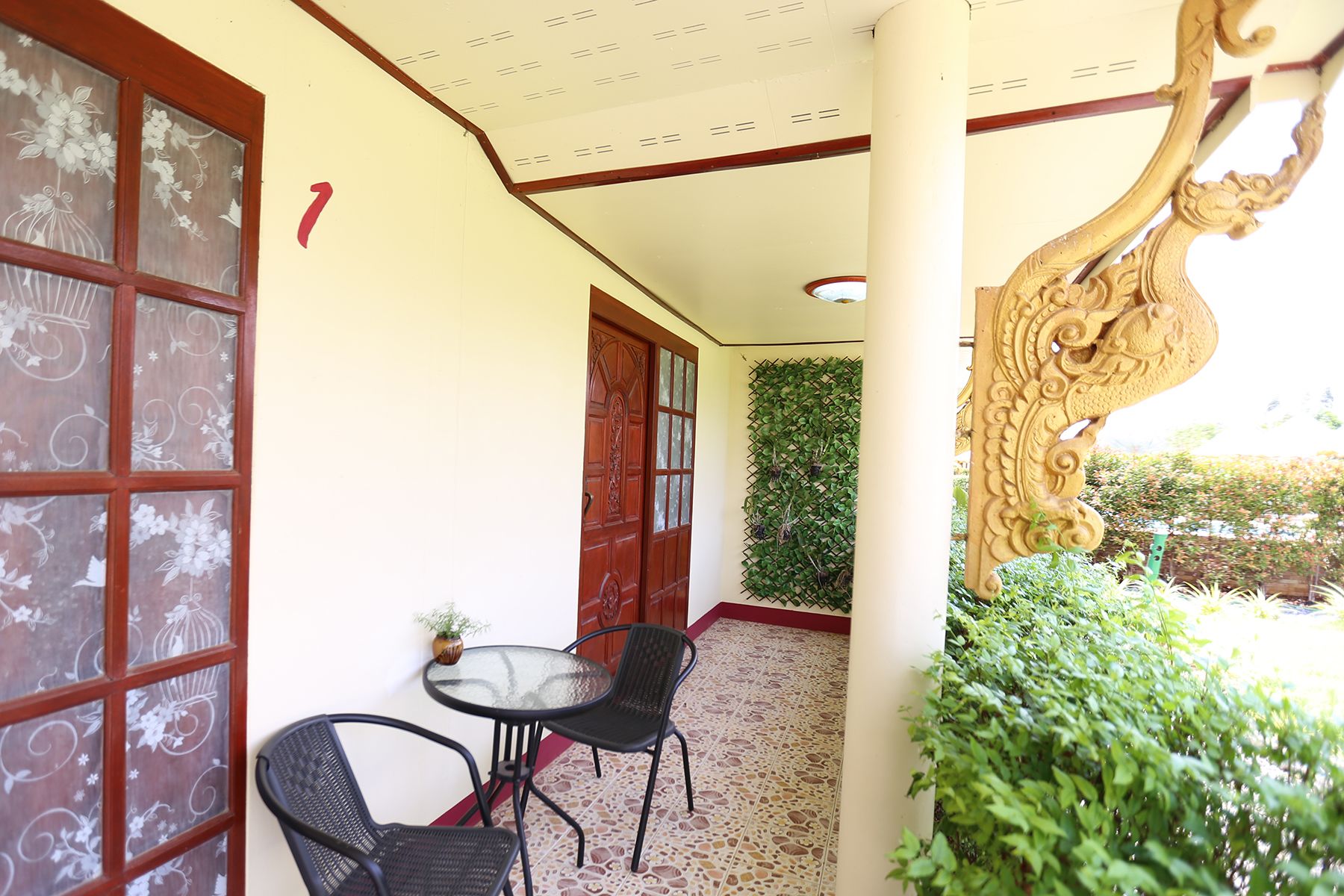 A covered outdoor seating area with a table and two chairs, a decorative wooden door, and a wall with a climbing plant.