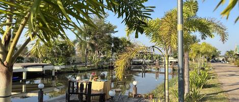 A riverside dining area with a wooden deck, tables, chairs, and a lamp post.