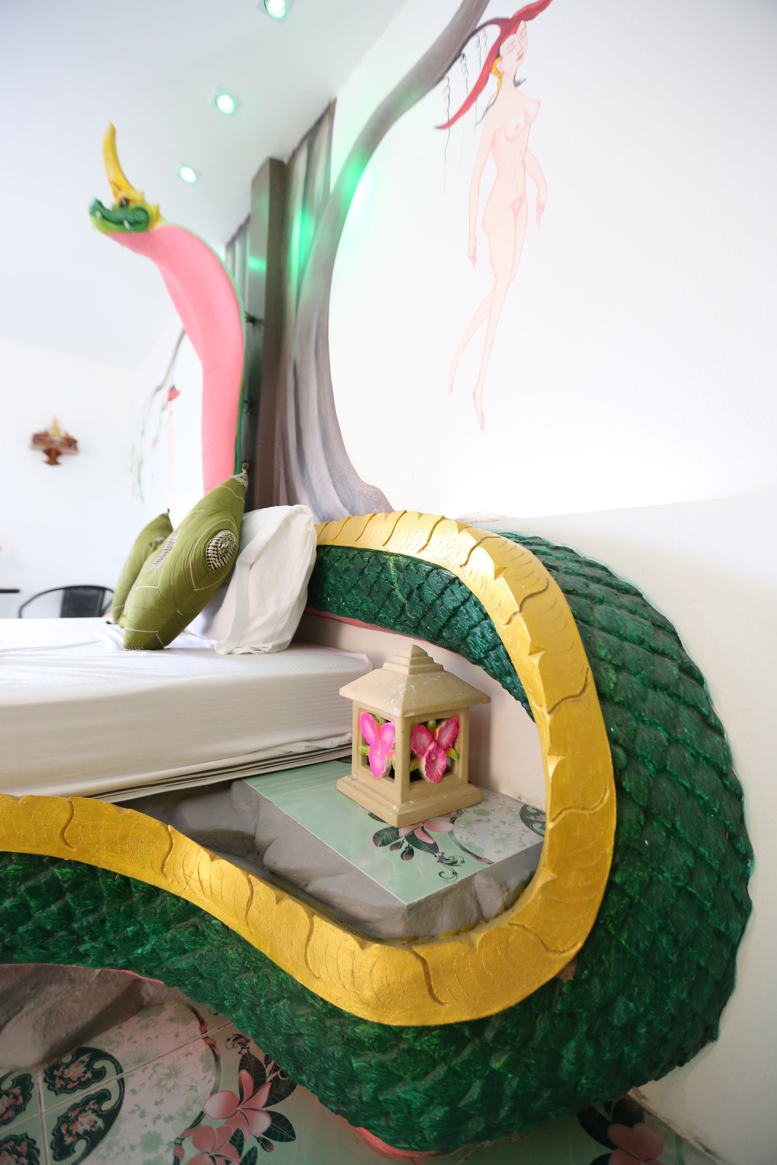 Una cama con diseño de serpiente verde y amarilla, un almohadón verde y un pequeño cofre de madera con flores rosas.