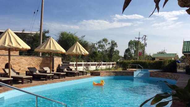 Piscina con sillas de descanso y sombrillas, rodeada por un muro de piedra y vegetación.