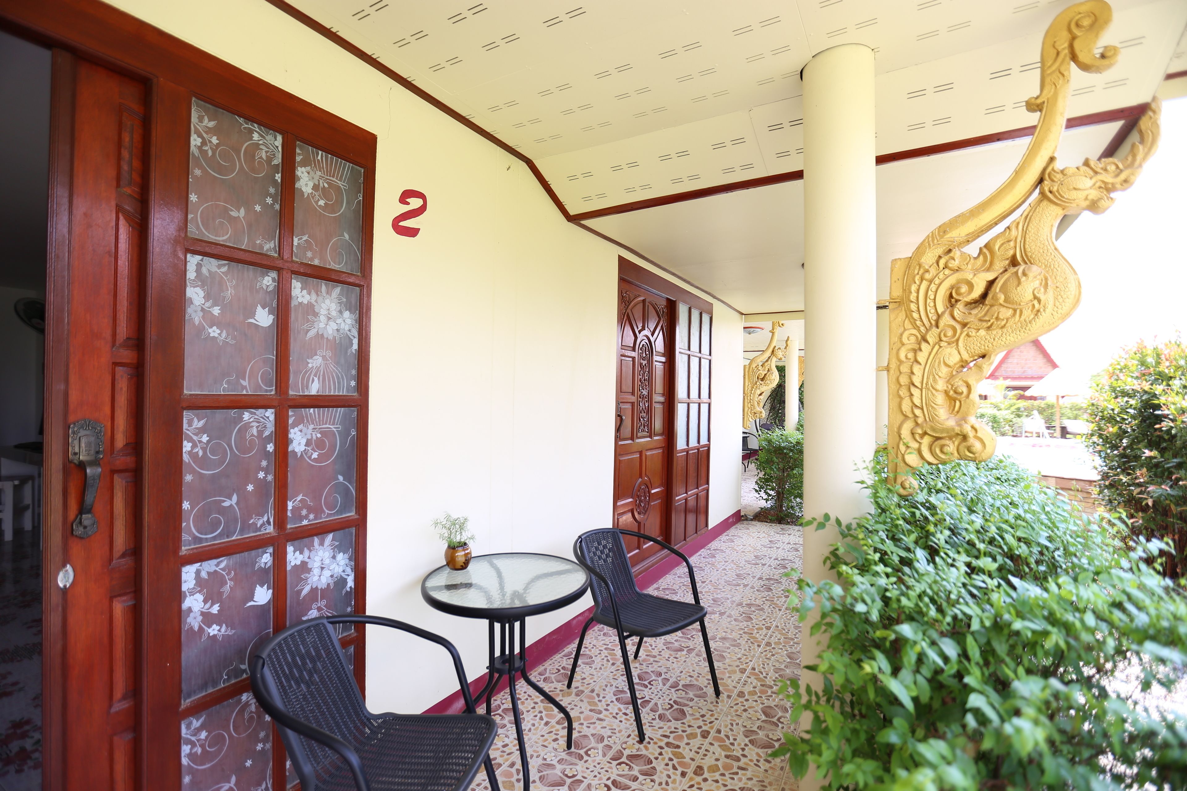 A covered outdoor area with a wooden door, two chairs, a small table, and a decorative golden sculpture.