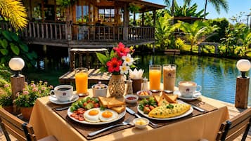 En frukostuppsättning med ägg, rostat bröd och juice på ett bord vid poolkanten, med utsikt över ett hus med en balkong.
