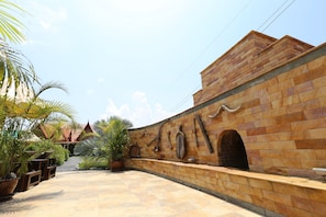Un patio con muro de piedra, plantas en macetas y un edificio tradicional al fondo.
