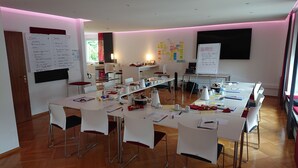 A conference room with white tables, chairs, and a whiteboard. - Hotel Bürger (Siegen)