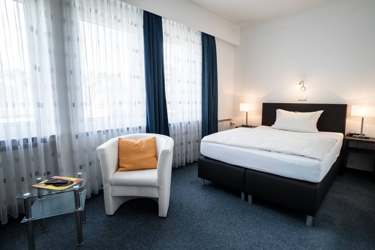 Una habitación de hotel con cama, una silla, una mesita y una ventana con cortinas.