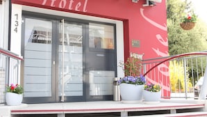A hotel entrance with a red facade, double doors, and a balcony with potted plants. - Hotel Bürger (Siegen)