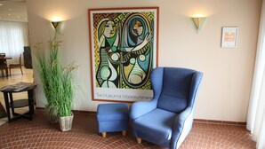 A modern art piece, a blue armchair, and a potted plant in a hotel lobby. - Hotel Bürger (Siegen)