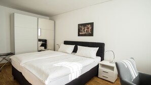 A modern bedroom with a large bed, a nightstand, a chair, and a wardrobe. - Hotel Bürger (Siegen)
