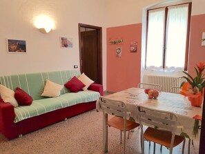 A cozy living room with a green sofa, a dining table with chairs, and a window with curtains.