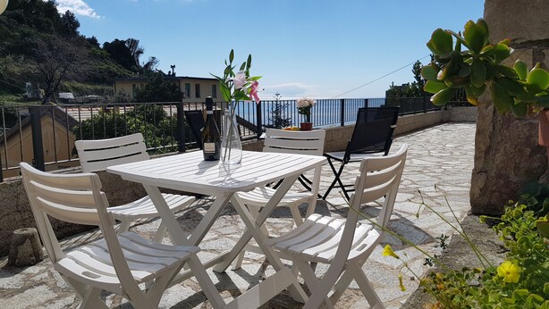 A terrace with a table and chairs, a bottle of wine, and a vase with flowers. - Augusto charming flat with sea view (Monterosso al Mare)