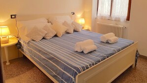 A neatly made bed with striped bedding and multiple pillows, a bedside lamp, and a window with curtains. - Augusto charming flat with sea view (Monterosso al Mare)